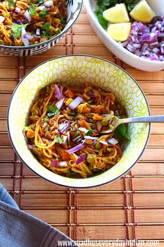 two bowls filled with noodles and vegetables on top of a bamboo mat next to a bowl of salad