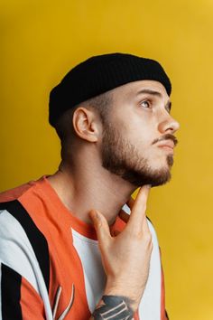 a man with a tattoo on his arm and hand near his face, standing in front of a yellow background