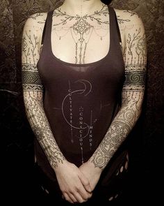 a woman with tattoos on her arm and chest standing in front of a dark background