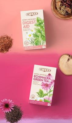 two boxes of green tea next to some pink flowers on a pink background with other items