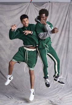 two young men in green and white outfits are jumping up into the air with their arms around each other