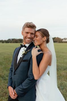 a bride and groom posing for a photo in front of an open field with green grass