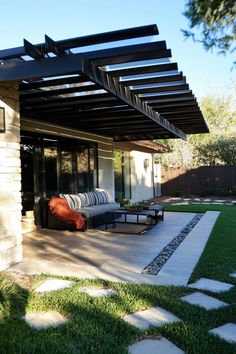 Modern patio with a pergola, outdoor seating, and a manicured lawn. Corrugated Tin, Reclaimed Wood Beams, Polycarbonate Panels, Retractable Canopy