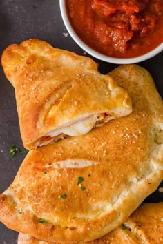 two pieces of bread with meat in the middle next to a bowl of tomato sauce