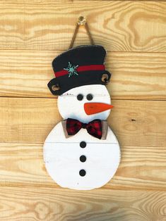 a snowman hanging on the side of a wooden wall wearing a hat and bow tie