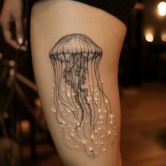 a woman's thigh with a jellyfish tattoo on it and pearls hanging from the legs