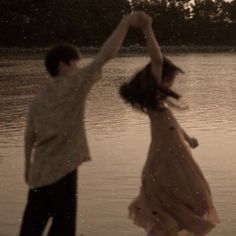 a man and woman are dancing in the water at sunset or sunrise, with trees in the background