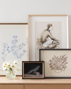 three framed pictures and two vases with flowers sit on a shelf next to each other