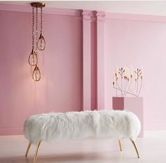 a white bench sitting in front of a pink wall next to a chandelier