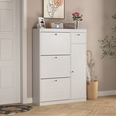 a white cabinet in a room next to a potted plant and vase with flowers