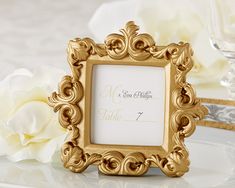 an ornate gold frame with a white flower on the side for a wedding place card holder