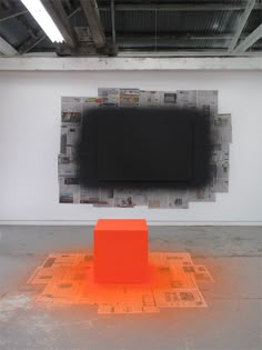 an orange cube sitting on top of a floor in front of a tv mounted to the wall