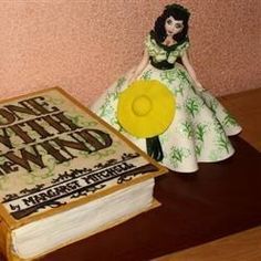 there is a cake with a book on it and a doll next to it that says, one day at the wind