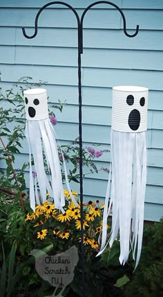 two paper cups with faces on them sitting in front of a flower pot filled with yellow flowers