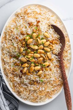 a white plate topped with rice and nuts next to a wooden spoon on a marble surface