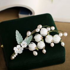 a white flower and leaf brooch sitting on top of a green velvet bag with pearls