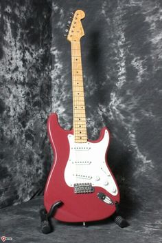 a red electric guitar sitting on top of a black background with a white neck and pick up