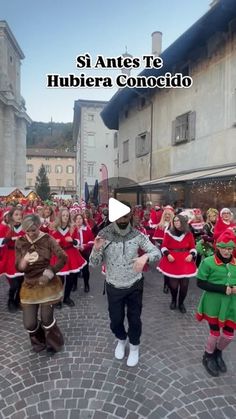 a group of people dressed in red and green are dancing on a cobblestone street