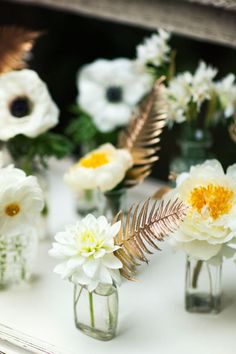 several vases filled with white and yellow flowers on top of a table in front of a mirror