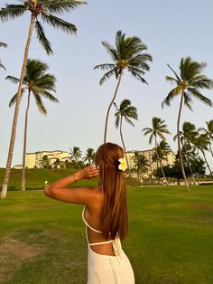 a woman standing in front of palm trees with her back to the camera and looking up