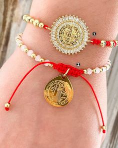 three bracelets with gold and red beads on the wrist, one featuring an image of jesus