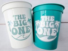 two plastic cups sitting next to each other on a white surface with the words the big one printed on them