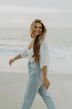 a woman walking on the beach with her hand in her pocket and smiling at the camera