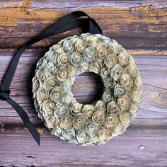 a wreath made out of rolled up paper flowers on a wooden surface with a black ribbon