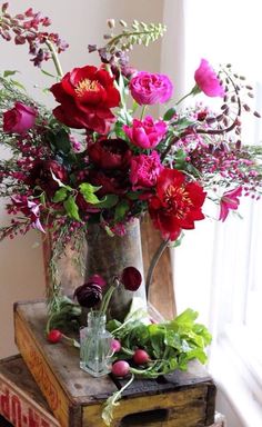 a painting of red flowers in a vase on a table next to an open book