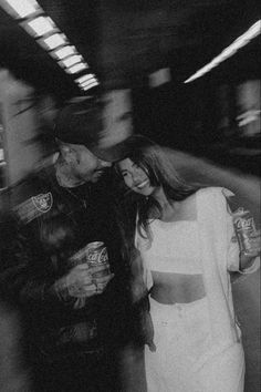 black and white photograph of man and woman walking in subway station with soda cans on their backs