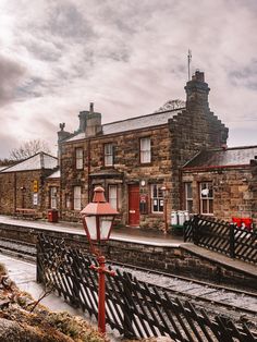 an old brick building with a red lamp post next to the train tracks in front of it