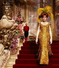 a woman in a gold dress is standing on some stairs with her hair blowing in the wind