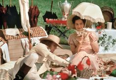 two women sitting on the ground with umbrellas over their heads and picnic tables in the background