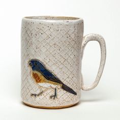 a ceramic mug with a bird painted on the outside of it's cup, sitting on a white surface