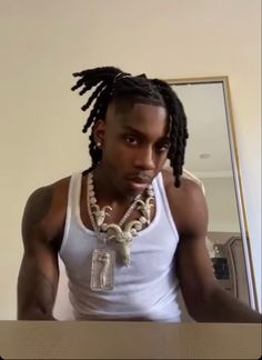 a man with dreadlocks wearing a white tank top and beads on his neck