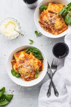 two white bowls filled with lasagna and spinach on top of a table