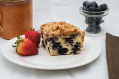 a piece of blueberry coffee cake on a plate with strawberries next to it