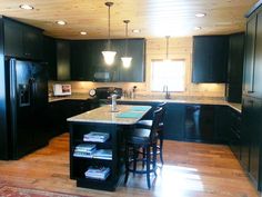 a kitchen with black cabinets and an island in the middle is lit by two pendant lights