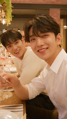 two young men sitting at a table with wine glasses