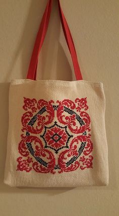 a red and white tote bag hanging on the side of a wall with an embroidered design