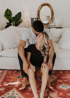 a man and woman sitting on top of a rug in front of a white couch