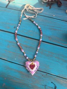 Handcrafted and adorned with beads, this lovely pink heart is accompanied by a string of matching beads and crystals. The leather straps allow for customizable wear, making this necklace a versatile addition to any outfit. Pink Adjustable Heart-shaped Necklace, Adjustable Pink Heart Necklaces, Adjustable Pink Heart-shaped Necklaces, Colorful Heart-shaped Beaded Jewelry, Valentine's Day Multicolor Heart Beaded Necklace, Valentine's Day Heart Shaped Multicolor Beaded Necklaces, Valentine's Day Adjustable Beaded Heart Pendant Necklace, Handmade Heart-shaped Jewelry For Festivals, Adjustable Beaded Necklace With Heart Pendant For Valentine's Day