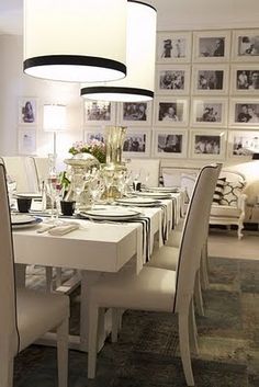 a dining room table with white chairs and pictures on the wall in the back ground