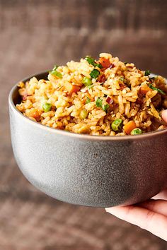 a hand holding a bowl filled with rice and peas