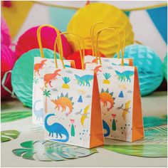 two paper bags with dinosaurs on them sitting on a table in front of colorful balloons