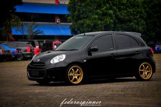 a small black car with gold rims parked in a parking lot