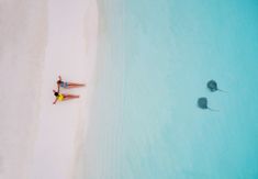 two people are laying on the beach with kites in the water and one person is lying down