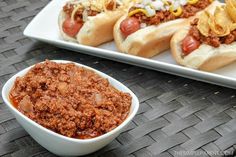 two hot dogs in buns with chili and cheese on them next to a plate