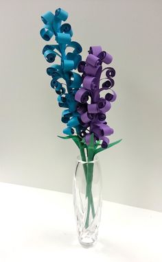 two purple and blue flowers in a clear vase on a white table top with water