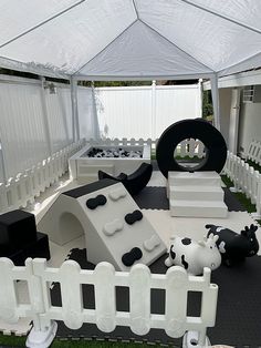 a white tent with black and white furniture in the grass next to a cow sculpture